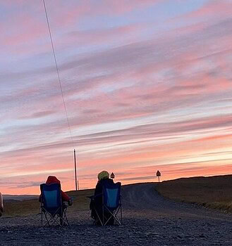 Us sitting in our camper charis outside the campervan admiring the 3 am sunrise in Iceland.