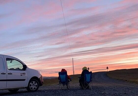 Us sitting in our camper charis outside the campervan admiring the 3 am sunrise in Iceland.