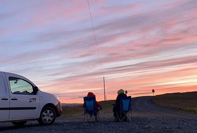 Us sitting in our camper charis outside the campervan admiring the 3 am sunrise in Iceland.