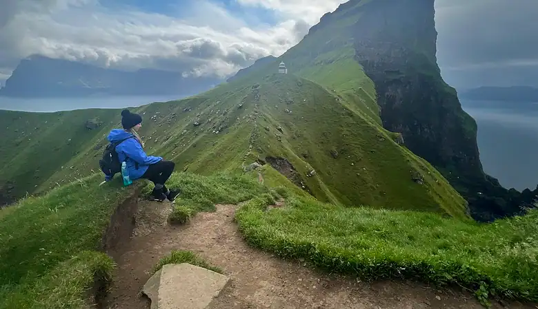 Me sitting along the Kallur lighthouse hike with dramatic cliff views in the background.
