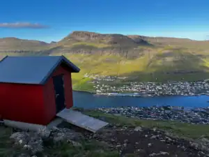 A little red barn with the town called Klaksvik in the background.